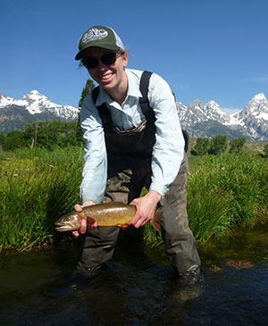 woman standing in a stream and holding a trout