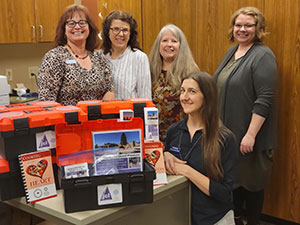 five people posing by a table with red and black plastic boxes on it