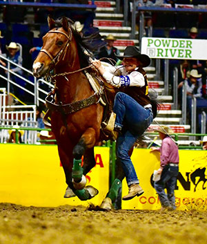 woman dismounting a running horse with a tying rope in her mouth