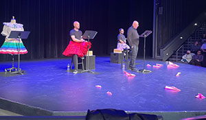 three people on a stage, reading to an audience