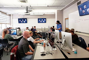 people at tables with computers listening to a lecturer