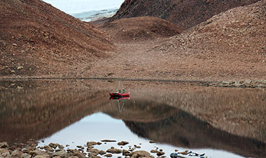 lake near hills with tiny boat on it
