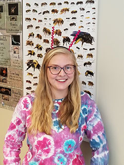 woman wearing antenna headpiece standing in front of a poster with insects
