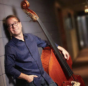 person with a string bass leaning against a wall