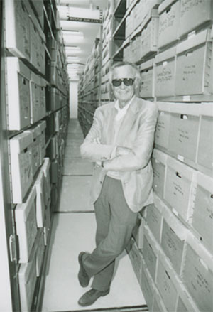 man leaning on boxes stored on rows of shelves