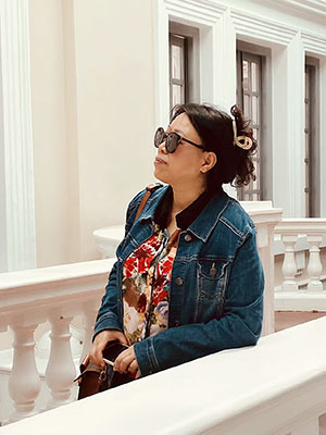 woman outside, leaning on a railing and looking towards a building