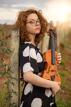 woman posing outside while holding a violin