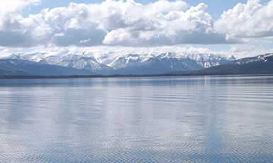 calm lake with snow-covered mountains and clouds in the background