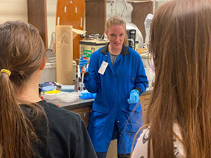 woman in a blue lab coat talks to two other people