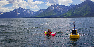person beside a marker in the middle of a mountain lake