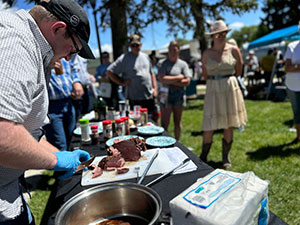 man outdoors at a festival cutting meat