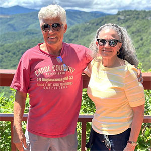 man and woman standing at a railing with mountains in the background