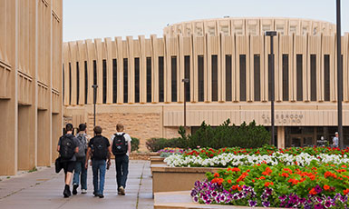 students walking by large buildings beside flower beds on campus