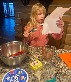 child looking at paper with cooking utensils and ingredients in front of her