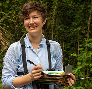 woman in woods working on papers in her hands