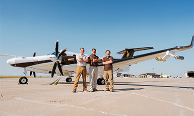 three people posing in front of an airplane