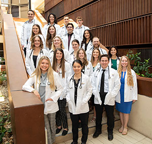 group of people with short white coats and stethoscopes posed on a staircase