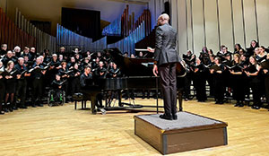 large group of singers on stage with a pianist and conductor