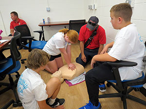 kids looking on as someone demonstrates CPR on a dummy