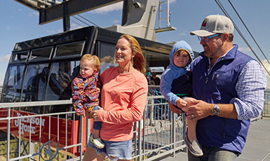 woman and man carrying small children past a ski lift gondola