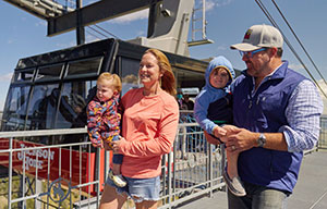 man and woman carrying small children beside a ski lift gondola
