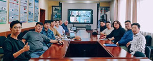 long table of people with a screen with more people at the far end