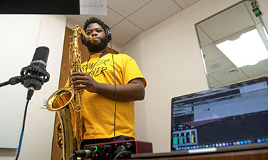 man playing saxophone with an open computer in the foreground