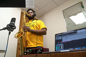 Man playing a saxophone with an open computer in the foreground