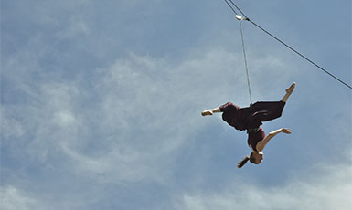 person suspended upside down from a wire while performing dance moves