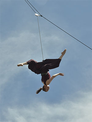 person suspended upside down from a wire while doing dance moves