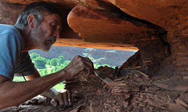 man lying on his front excavating something under a rock shelf