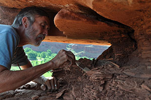 man lying on his front excavating something under a rock shelf