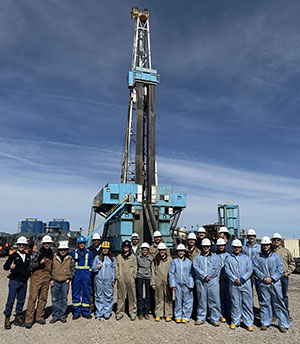 group of people wearing hard hats standing in front of a drilling rig