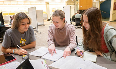 three young women studying together at a table