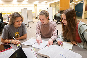 three young women with notebooks and textbooks working together at a table