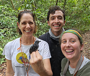 three people posing in a forest, one holding a bird