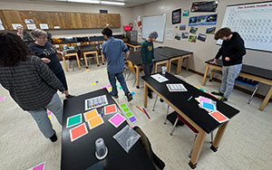 people moving around in a room with colored squares of paper on lab tables
