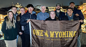 group of people holding up a One Wyoming flag with a Chinese city in the background
