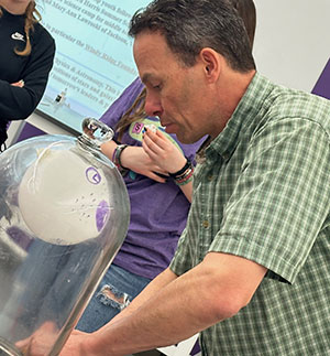 man looking into a large glass bell jar with something white inside it