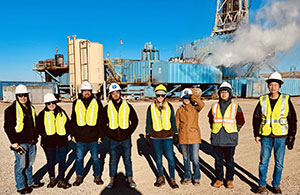 group of people wearing hard hats and posing in front of a drill site