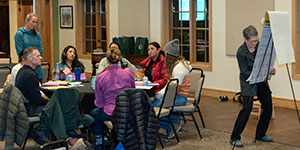 group of people at a table while someone else writes on an easel