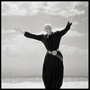 black and white photo of a woman with arms out in front of a body of water