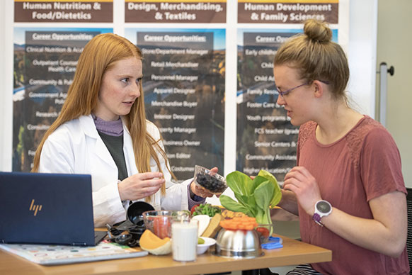 two women talking with different foods on a table in front of them