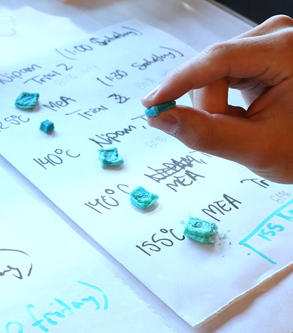 person's hand with a small amount of material with other small samples on a labeled sheet of paper below