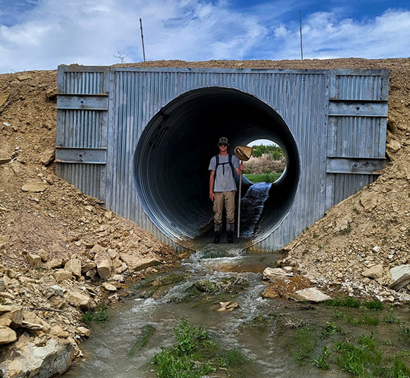 person standing inside a huge drainage pipe with a stream coming out of it