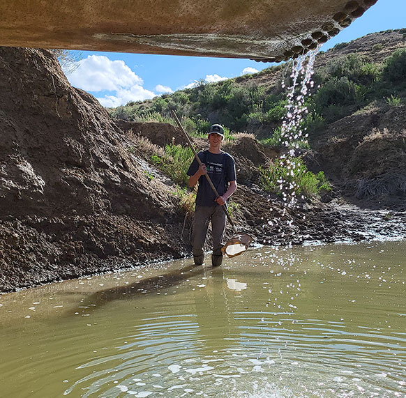 man wading into a pool of water with a pipe dripping more water into it