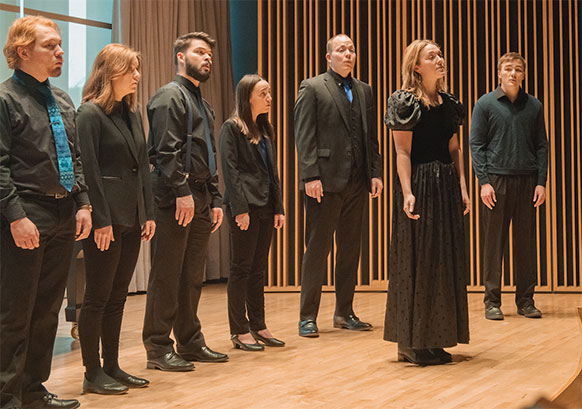 people wearing black standing on a stage and singing