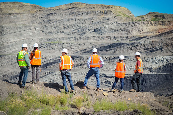 people in safety vests and hard hats looking into an open pit mine