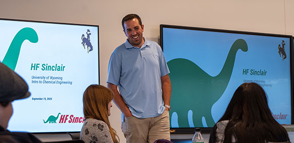 man standing at the front of a classroom with screens advertising Sinclair behind him