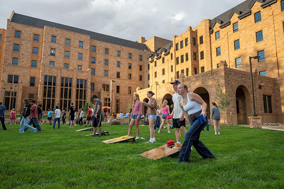 students playing games on grassy area by dorms
